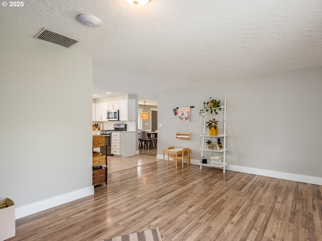living room featuring visible vents, light wood-style flooring, baseboards, and a textured ceiling