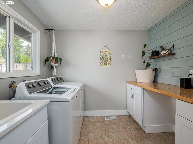 washroom featuring visible vents, baseboards, separate washer and dryer, cabinet space, and a textured ceiling