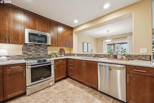 kitchen with pendant lighting, a sink, tasteful backsplash, stainless steel appliances, and light stone countertops