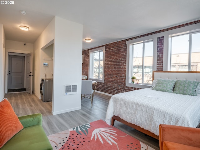 bedroom featuring washing machine and clothes dryer, brick wall, and light wood-type flooring