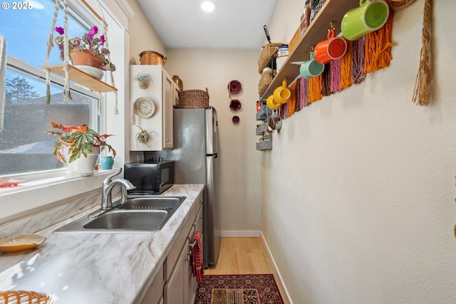 kitchen featuring baseboards, a sink, light countertops, light wood-style floors, and black microwave