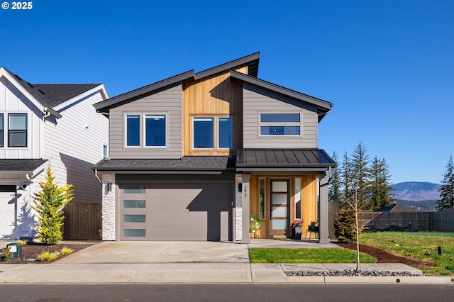 modern home featuring an attached garage, a mountain view, fence, concrete driveway, and a standing seam roof