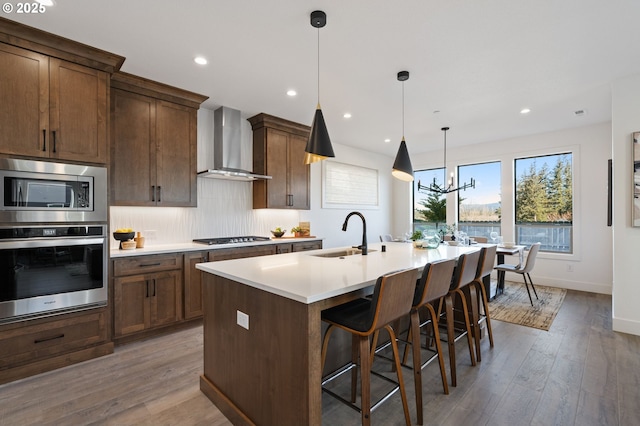 kitchen with appliances with stainless steel finishes, a kitchen island with sink, a sink, wall chimney range hood, and a kitchen bar