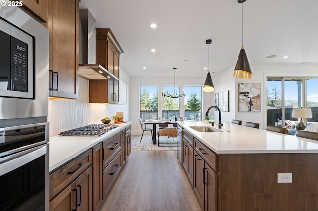 kitchen with stainless steel appliances, wood finished floors, a sink, light countertops, and wall chimney range hood