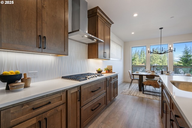 kitchen featuring stainless steel gas cooktop, light countertops, wall chimney range hood, decorative backsplash, and hardwood / wood-style floors