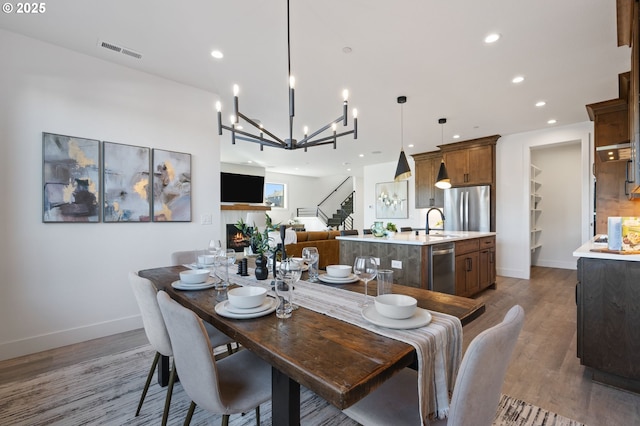 dining space featuring a warm lit fireplace, recessed lighting, wood finished floors, visible vents, and stairs