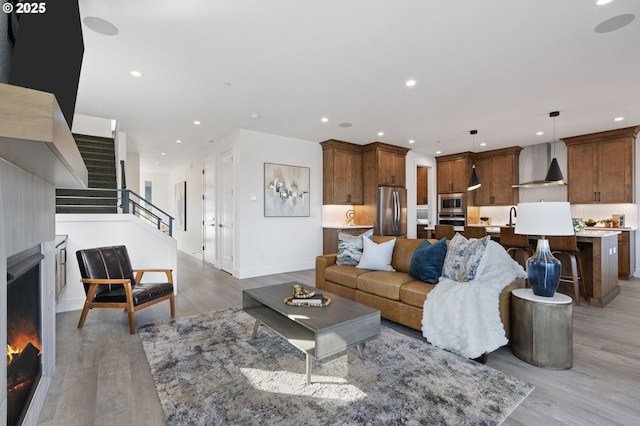 living area featuring recessed lighting, baseboards, stairs, a lit fireplace, and light wood finished floors