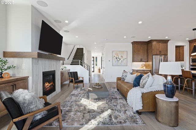 living area featuring recessed lighting, light wood-style flooring, stairs, and a glass covered fireplace