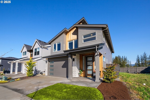 view of front of house featuring concrete driveway, stone siding, an attached garage, fence, and board and batten siding