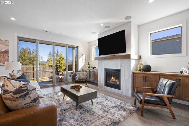 living room featuring light wood-style flooring, a glass covered fireplace, visible vents, and recessed lighting