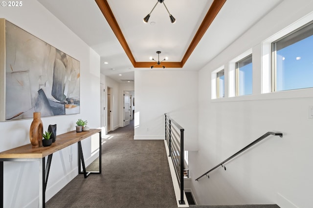 corridor featuring a tray ceiling, recessed lighting, dark carpet, an upstairs landing, and baseboards