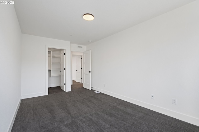 unfurnished bedroom featuring dark colored carpet, a walk in closet, visible vents, and baseboards