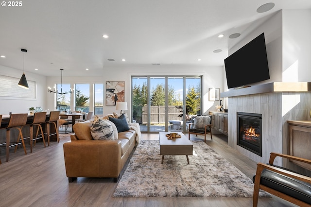 living area with recessed lighting, a chandelier, wood finished floors, and a glass covered fireplace