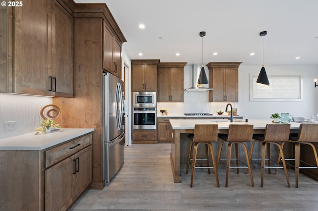 kitchen featuring stainless steel appliances, a sink, light wood-style floors, wall chimney range hood, and a kitchen bar