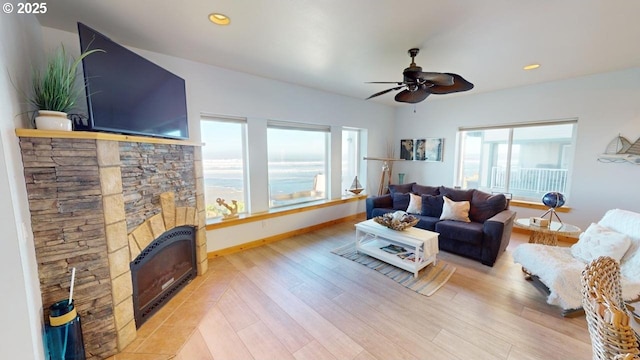 living room with light hardwood / wood-style flooring, a stone fireplace, heating unit, and ceiling fan