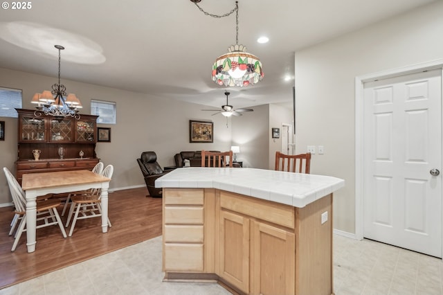 kitchen with a kitchen island, ceiling fan with notable chandelier, tile countertops, light brown cabinetry, and hanging light fixtures