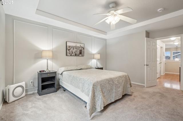 bedroom featuring a raised ceiling, light carpet, and ceiling fan