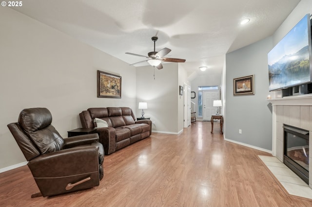 living room featuring a tile fireplace, ceiling fan, and light hardwood / wood-style floors