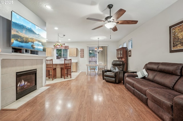 living room featuring ceiling fan with notable chandelier, a fireplace, and light wood-type flooring