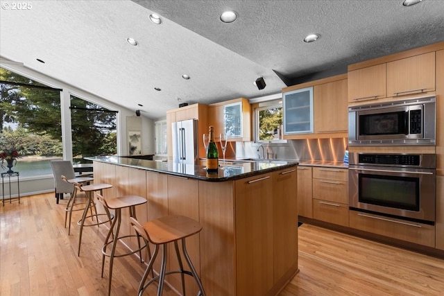 21047 NE Interlachen Ln, Fairview, OR 97024 - kitchen with stainless steel appliances, light wood-style floors, glass insert cabinets, a kitchen breakfast bar, and lofted ceiling