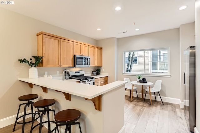 18445 SW Stepping Stone Dr Unit 16, Beaverton, OR 97003 - kitchen featuring stainless steel appliances, light brown cabinetry, a peninsula, baseboards, and a breakfast bar area