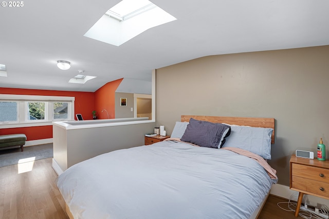 bedroom with baseboards, lofted ceiling with skylight, and wood finished floors