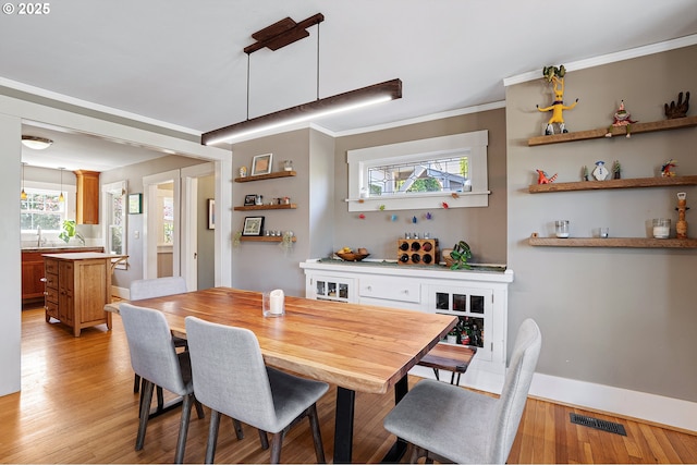 dining space with crown molding, baseboards, light wood-type flooring, and visible vents