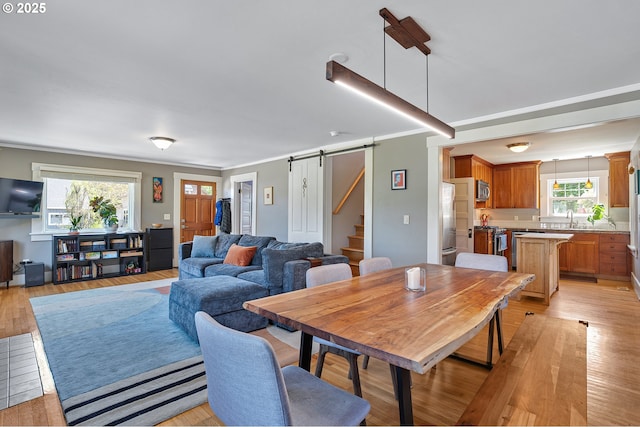 dining area featuring a barn door, ornamental molding, and light wood-style floors