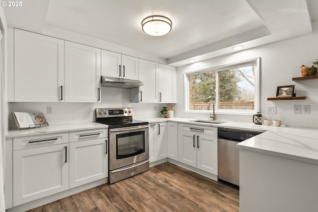 kitchen with under cabinet range hood, a sink, white cabinetry, appliances with stainless steel finishes, and dark wood-style floors