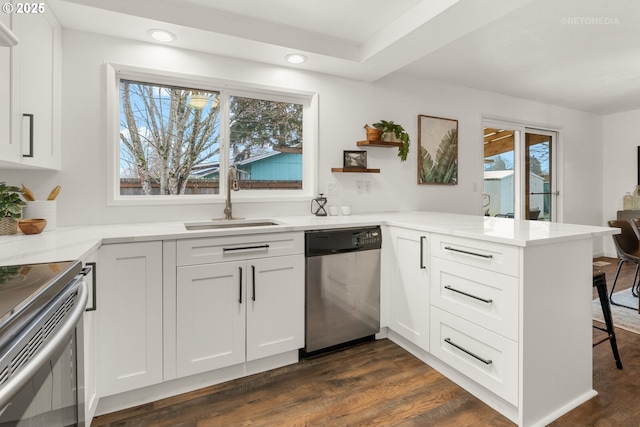 kitchen with a peninsula, a sink, white cabinetry, appliances with stainless steel finishes, and dark wood finished floors