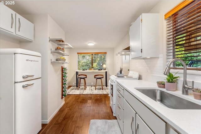 kitchen featuring range hood, white cabinetry, sink, backsplash, and white appliances