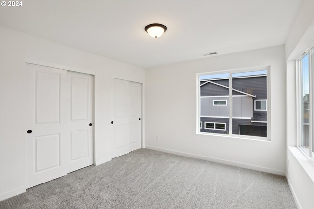 unfurnished bedroom featuring multiple closets, visible vents, carpet floors, and baseboards