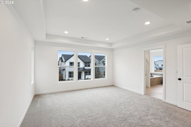 spare room with baseboards, a tray ceiling, and light colored carpet