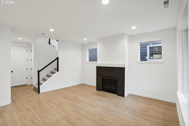 unfurnished living room featuring light wood-style flooring, stairway, a tiled fireplace, and visible vents
