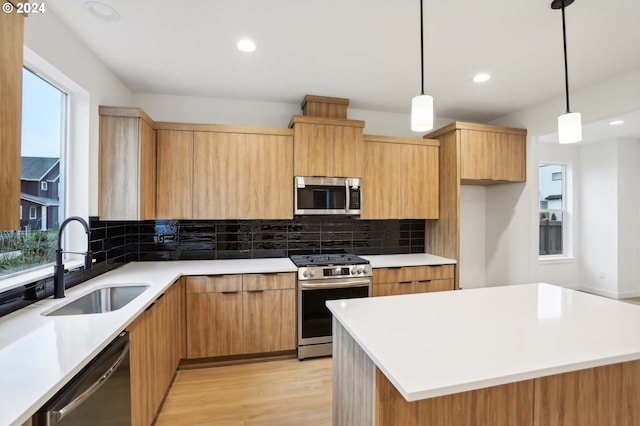 kitchen featuring stainless steel appliances, a kitchen island, a sink, light countertops, and pendant lighting