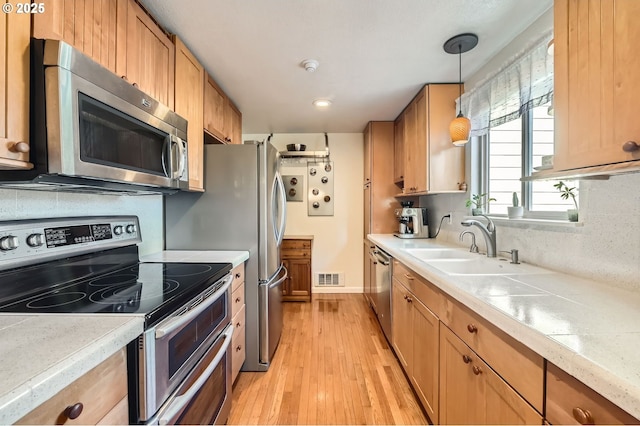 2433 NE Saratoga St, Portland, OR 97211 - kitchen featuring visible vents, a sink, light wood finished floors, appliances with stainless steel finishes, and hanging light fixtures