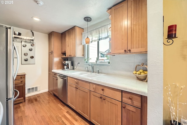 2433 NE Saratoga St, Portland, OR 97211 - kitchen with appliances with stainless steel finishes, a sink, light wood finished floors, decorative backsplash, and visible vents