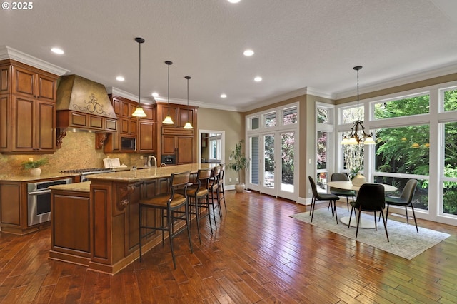 kitchen with brown cabinetry, ornamental molding, premium range hood, and stainless steel appliances