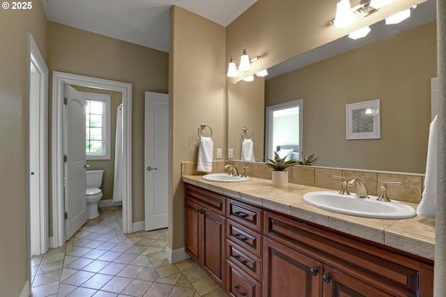 full bathroom featuring double vanity, toilet, a sink, and tile patterned flooring
