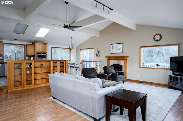 living room featuring a fireplace, rail lighting, ceiling fan with notable chandelier, and light hardwood / wood-style flooring