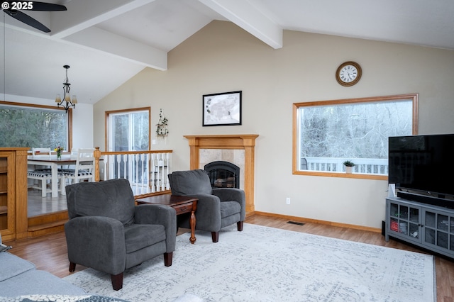 living room featuring a tile fireplace, lofted ceiling with beams, ceiling fan with notable chandelier, and hardwood / wood-style flooring