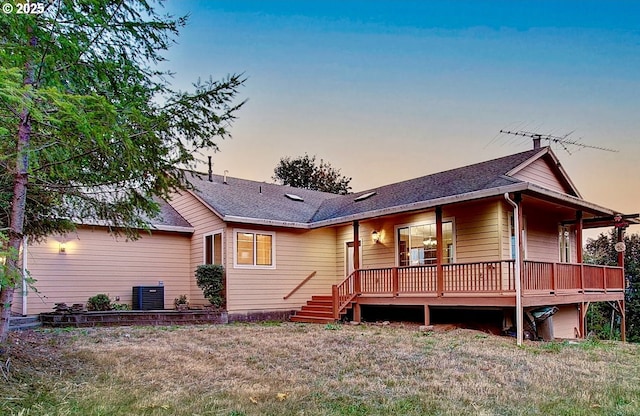 back house at dusk featuring a deck, a yard, and central AC unit