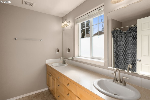 full bath featuring double vanity, visible vents, baseboards, and a sink