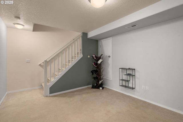 finished below grade area featuring carpet, baseboards, visible vents, stairs, and a textured ceiling