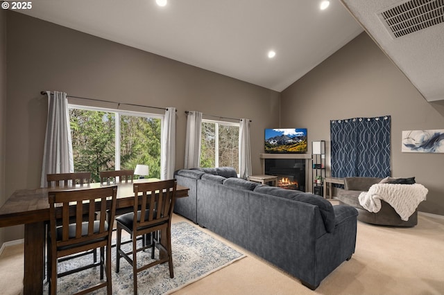 carpeted living area featuring visible vents, high vaulted ceiling, a glass covered fireplace, recessed lighting, and baseboards