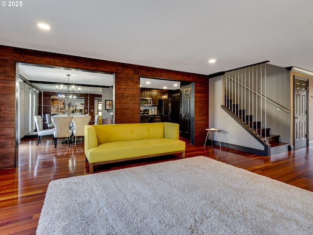 unfurnished living room featuring stairs, wood walls, wood finished floors, and an inviting chandelier