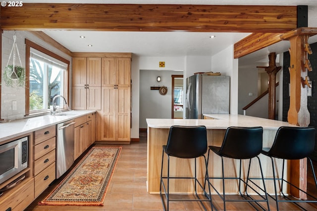 kitchen featuring light brown cabinetry, sink, a center island, appliances with stainless steel finishes, and beamed ceiling