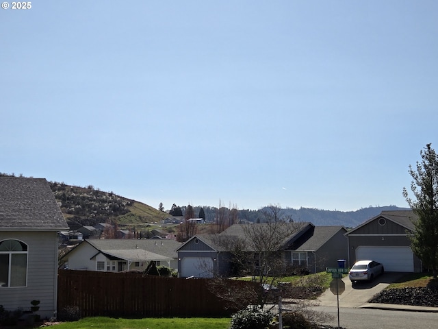 ranch-style home featuring fence, a residential view, concrete driveway, a garage, and a mountain view