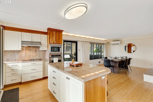 kitchen featuring appliances with stainless steel finishes, light hardwood / wood-style flooring, white cabinetry, a kitchen island, and a wall mounted AC