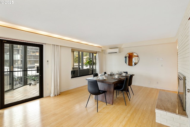 dining room featuring a fireplace, a wall mounted air conditioner, and light hardwood / wood-style flooring